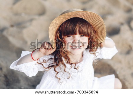 Cheerful little girl on the beach background looks at the camera.