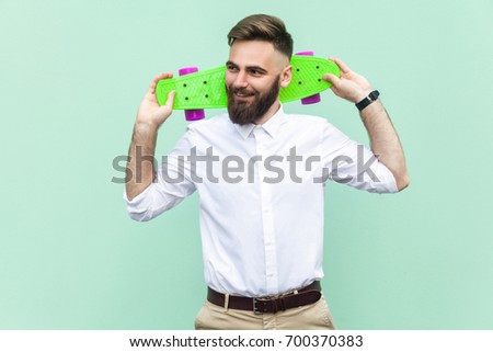 Young adult businessman, holding under head his skate,looking left and toothy smiling. Light green background. Studio shot