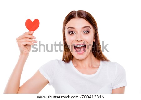 Love concept. Very excited young brown-haired girl, holding small red paper heart, in white outfit, on white background