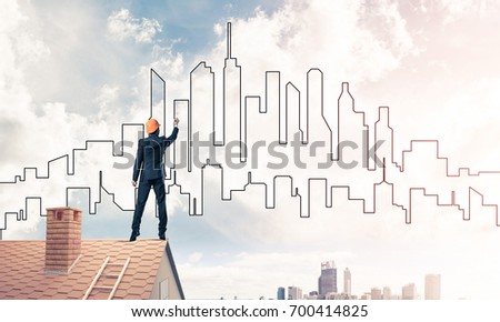 Engineer man standing with back on house roof and drawing city. Mixed media