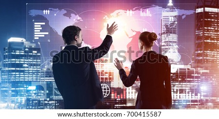 Two business people standing with back and working together with virtual screen