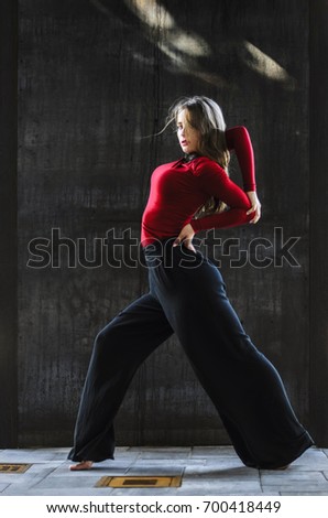 girls dancing in the city. doing gymnastic stunts . dressed in black pants and a red sweater. on a background of black wall.