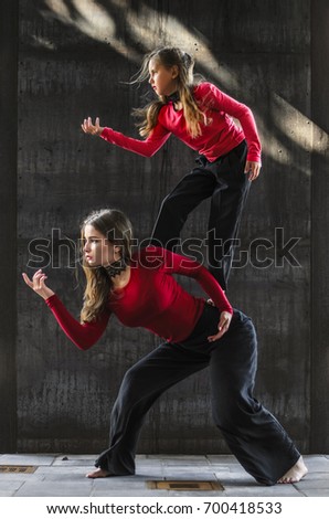 girls dancing in the city. doing gymnastic stunts . dressed in black pants and a red sweater. on a background of black wall.