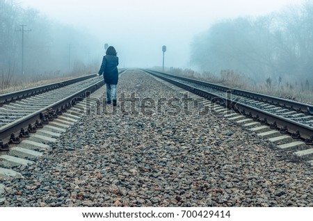 the girl walks on rails in the fog. waiting for the train, a teenager wanders