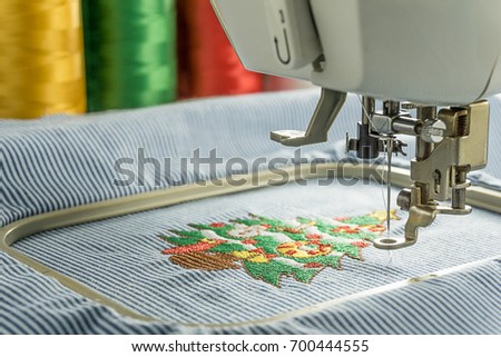 Picture of workspace embroidery machines finish working cartoon christmas tree on stripes fabric take in medium close up shot 