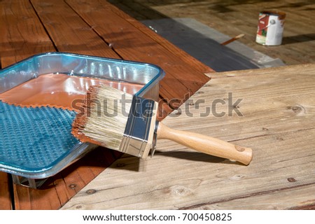 Diy concept of varnishing a wooden floor or exterior deck with a plastic tray and paintbrush on the corner angle with only one half painted Royalty-Free Stock Photo #700450825