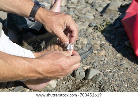 Man putting a sticking plaster on his toe to treat a blister caused by his hiking boots or other small injury in a close up view of his hands Royalty-Free Stock Photo #700452619
