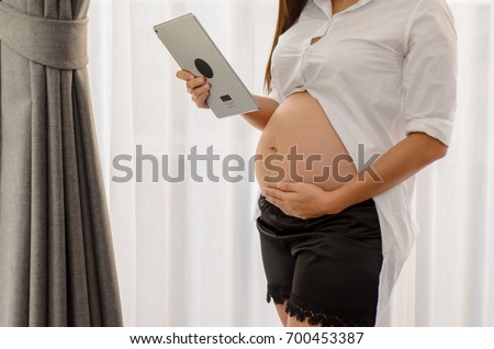 Pregnant woman is playing a tablet at her house. Planning ahead of child