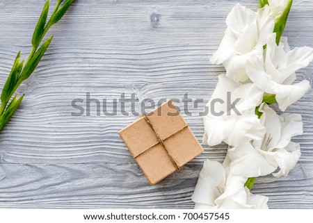 Celebration accessories. Box in kraft paper near flower gladiolus on light wooden table top view copyspace
