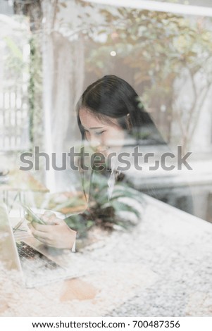 Portrait of happy young business Asian woman relaxing and using smartphone after finished project behind the glass wall at coffee shop.