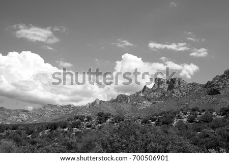 Black and white photo of huge puffy white monsoon clouds framing the Catalina mountains mesas on a sunny day in the tucson arizona desert 