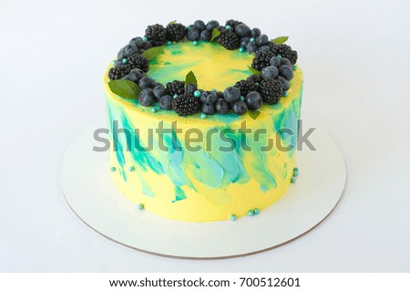Cake with whipped yellow and green cream, fresh blueberries, blackberry and leaves, decorated with blue confectionery sprinkles. Picture for a menu or a confectionery catalog.