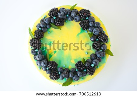 Cake with whipped yellow and green cream, fresh blueberries, blackberry and leaves, decorated with blue confectionery sprinkles. Picture for a menu or a confectionery catalog. Top view.