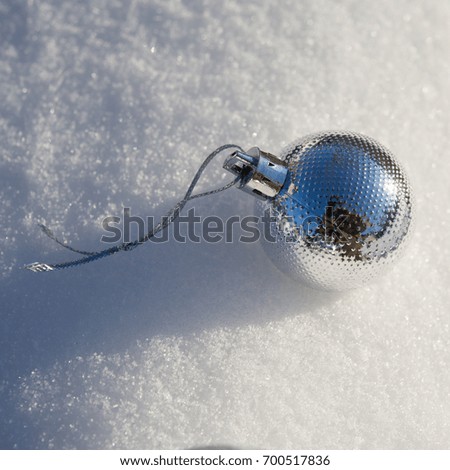 Christmas toy ball lies on the snow in the sunlight. Festive background.