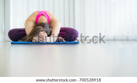 Front view of young woman exercising stretching back yoga pose on mat in an indoor gym with copy space. Healthy lifestyle and wellness concept.