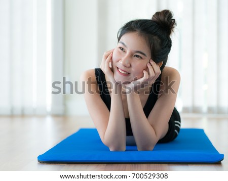 Young happy woman relaxing on yoga mat in fitness gym. Healthy lifestyle and wellness concept.