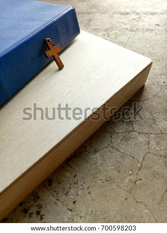 Old Christian Cross leaning blue cover Bible book on wooden background and vintage grunge  floor with morning sunlight, selective focus with copy space