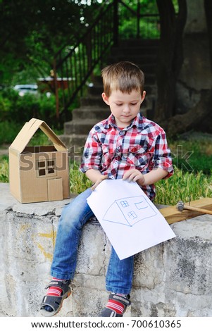 Baby boy with a picture with a painted house sits on the background of a toy cardboard house