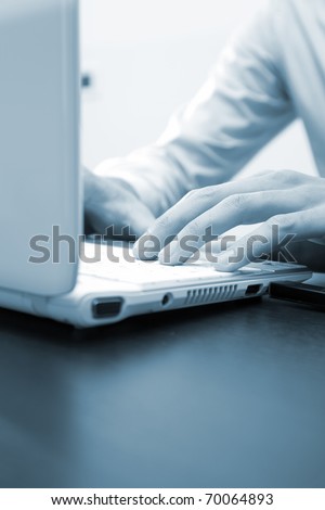Male hands typing on a laptop, blue toned image
