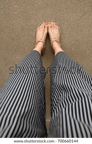 Feet Woman Wear Sandals and Black Pants. Female Standing on The Cement Background Great For Any Use.