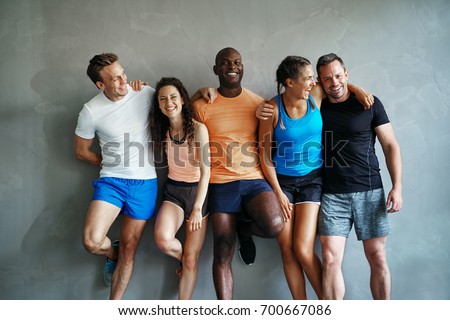 Smiling group of friends in sportswear laughing together while standing arm in arm in a gym after a workout