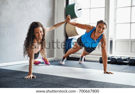 Two smiling young female friends in sportswear high fiving each other while doing pushups together on the floor of a gym Royalty-Free Stock Photo #700667800