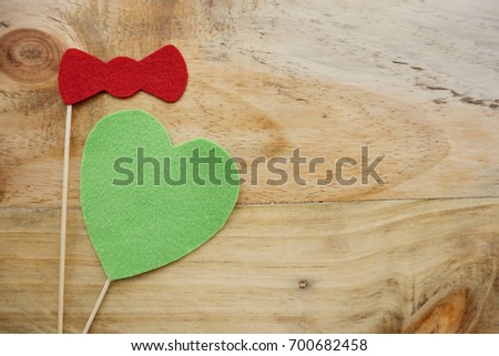 Top or flat lay view of Photo booth props a green heart and a red bow tie on a wooden background flat lay. Birthday parties and weddings.