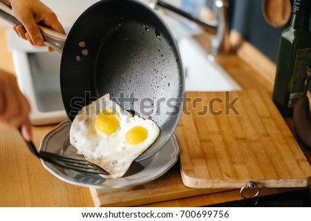 Two fried eggs in a pan with olive oil. Girl's hand holding a frying pan with scrambled eggs. Royalty-Free Stock Photo #700699756