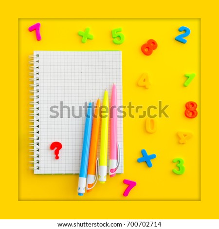 Notebook with multicolored numerals and pens on yellow background. Overhead shot. Copy-space composition. Back to school concept.