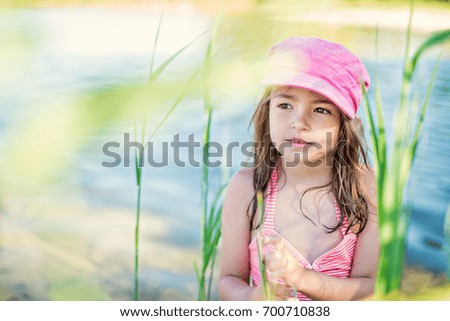 Portrait beautiful kid girl standing In the reed in lake in summer sunny day