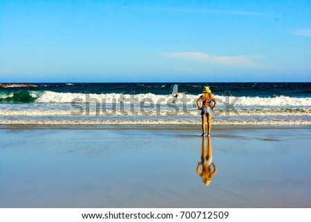 Landscape photograph of beautiful beach. A lady standing on the beach looking out to the sea. Her shadow reflect on the wet sand. Blue clear sky on background.