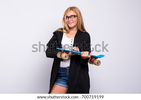 a young girl with the penny board in the Studio. woman in glasses standing with a small blue skateboard, on a white background
