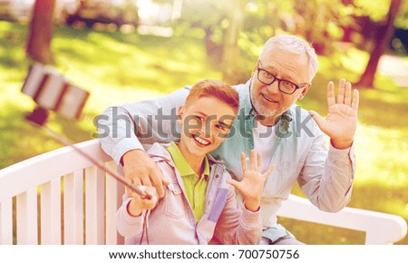 family, generation, technology and people concept - happy grandfather and grandson taking picture with smartphone selfie stick at summer park