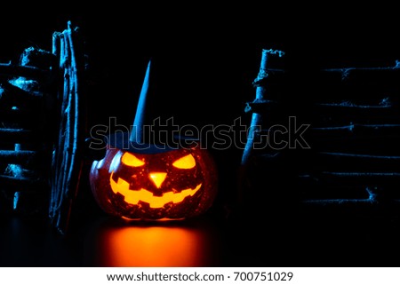 Glowing carved pumpkin in hat lying on surface in darkness background of decorative wooden fence