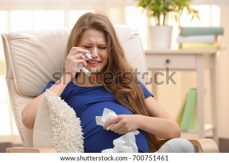 Emotional pregnant woman sitting in arm chair and crying. Pregnancy hormones concept Royalty-Free Stock Photo #700751461