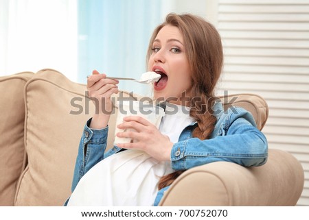 Emotional pregnant woman sitting on sofa and eating ice-cream. Pregnancy hormones concept Royalty-Free Stock Photo #700752070