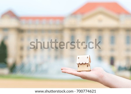Man hand holding a wooden model house over the blurred building