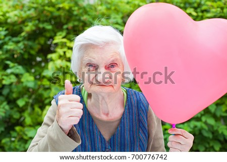 Picture of a cute elderly lady celebrating birthday with a heart shaped balloon in the park, outdoor
