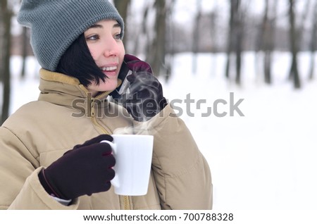 Pretty young girl wear warm winter hat and coat. Fun brunette female model walk outside with smartphone and coffee cup in cold weather. Smiling happy model posing. Good holiday weather