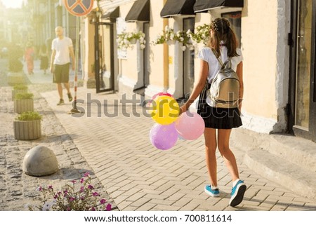 Back view,  Girl teenager high school student with balloons, in school uniform with glasses goes along the city street. Start of classes.
