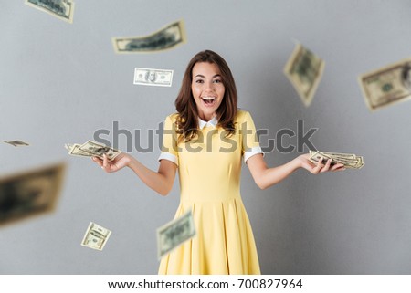 Picture of happy young caucasian lady standing over levitate money over grey background. Looking camera.