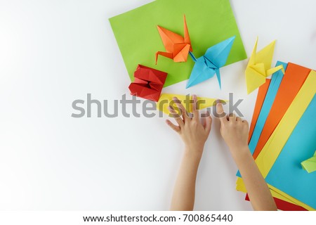 Children's hands do origami from colored paper on white background. lesson of origami Royalty-Free Stock Photo #700865440