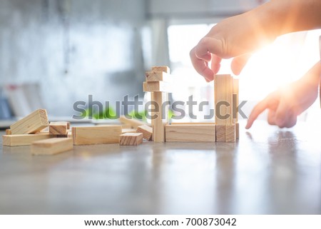 Hand of kid playing a blocks wood tower game of architectural project with sun flare and blur background .Selected focusing . Royalty-Free Stock Photo #700873042