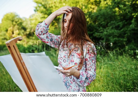 Portrait of an attractive young woman in long dress painting with watercolor in nature.