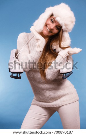Winter sport activity concept. Girl wearing furry hat and warm clothes holding ice skate, blue background studio shot.