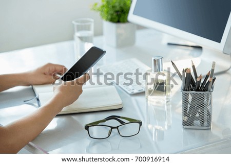 Close-up of female hands using smart phone while working on computer at modern office interior