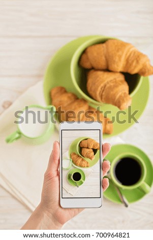 Female hand holding smart phone with picture of coffee with croissants. Selective focus.