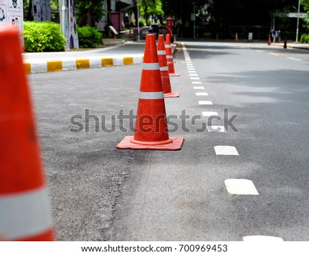 bright orange traffic cones standing in a row on asphalt. concrete sidewalk with yellow and white traffic sign.