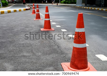 bright orange traffic cones standing in a row on asphalt. concrete sidewalk with yellow red and white traffic sign.