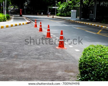 bright orange traffic cones standing in a row on asphalt. concrete sidewalk with yellow red and white traffic sign.